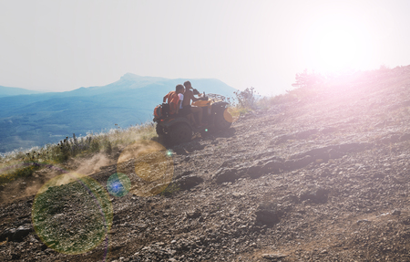 Three young guys are driving an ATV up a mountain roadの写真素材