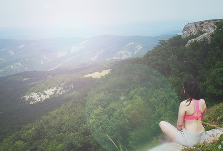 A young girl sits on edge cliff and looking at mountain landscapeの写真素材