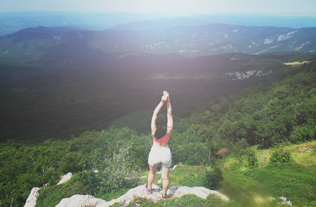 A young girl sits on edge cliff and looking at mountain landscapeの写真素材