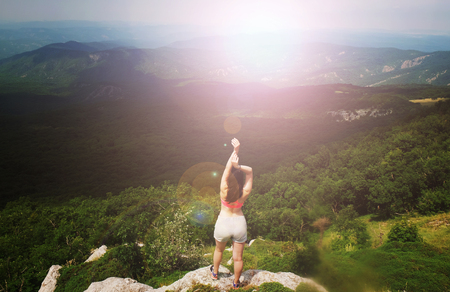 A young girl sits on edge cliff and looking at mountain landscapeの写真素材