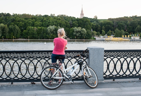 A young girl with a bicycle is standing on the embankment in Moscow.の写真素材