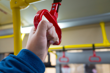 The man's hand holds onto the red handle of the handrail in public transportの写真素材