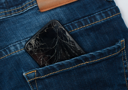 Mobile phone with a broken screen in the pocket of blue jeans.の写真素材