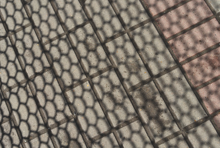 The texture of the shadow of the metal mesh on the concrete paving slabs.の写真素材