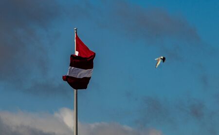 Bordeaux white flag of Latvia against a cloudy skyの写真素材