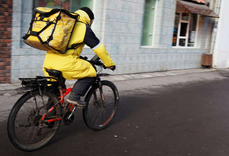 OLYMPUS DIGITAL CAMERAMarch 10, 2019 Moscow, Russia An employee of the Yandex Food delivery service rides a bicycle on a street in Moscow.のeditorial素材