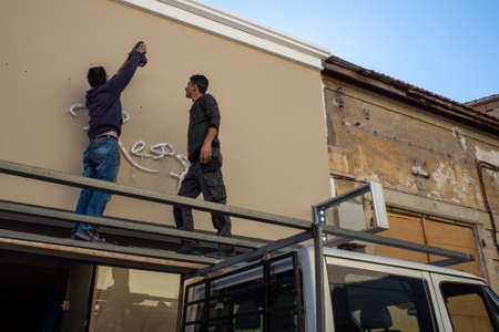 April 22, 2019, Limassol, Cyprus. Two workers are installing a cafe sign on a street in the city of Limassol.のeditorial素材