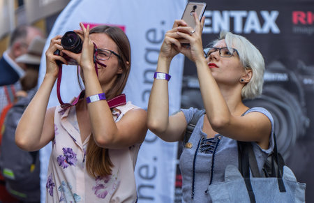 August 18, 2018. Moscow, Russia. Two girls on a busy street are taking pictures with their phones and cameras of something interesting above.のeditorial素材