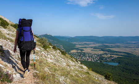 A girl with a large blue backpack climbs a trail in the mountains of the Crimean peninsula.の写真素材