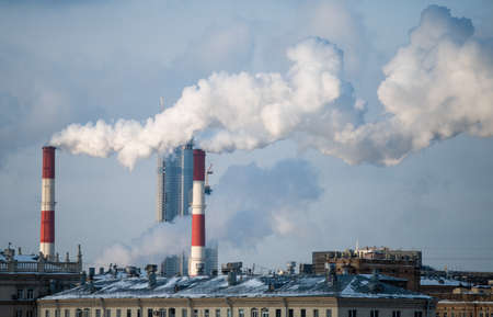 Smoke from the chimneys of a combined heat and power plant against the backdrop of a skyscraper under construction on a frosty winter day.の写真素材