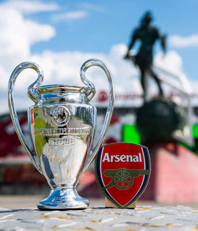 June 14, 2021, London, UK. Arsenal FC football club emblem and the UEFA Champions League Cup against the backdrop of a modern stadium.のeditorial素材