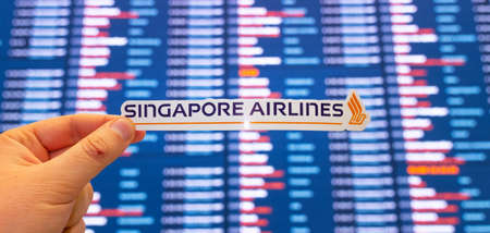 December 11, 2021 Singapore. The emblem of Singapore Airlines against the background of an electronic scoreboard with flight schedules at the international airport.のeditorial素材