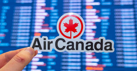 December 11, 2021 Montreal, Canada. The emblem of the Air Canada airline against the background of an electronic board with a flight schedule at an international airport.のeditorial素材