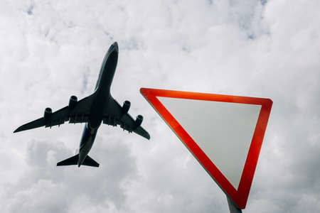 Road sign "Give way" against the background of the silhouette of a flying plane.の写真素材