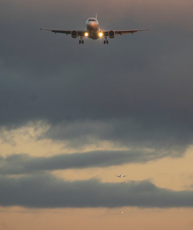 The silhouette of a passenger plane coming in for landing against the backdrop of the sunset sky.の写真素材