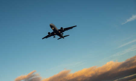 The silhouette of a passenger plane coming in for landing against the backdrop of the sunset sky.
