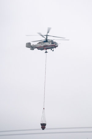 A fire helicopter carries a container of water to extinguish a fire in a production building
