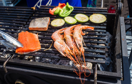 A cook cooks trout steaks and tiger prawns on coals in an outdoor cafe.の写真素材