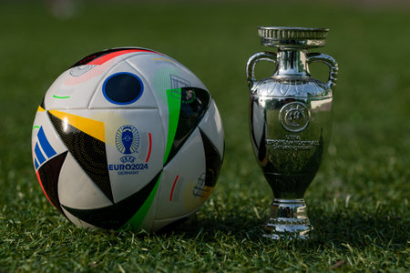 June 14, 2024, Berlin, Germany. The official ball and cup of the European Football Championship 2024 Adidas EURO24 Fussballiebe on the green lawn of the stadium.のeditorial素材