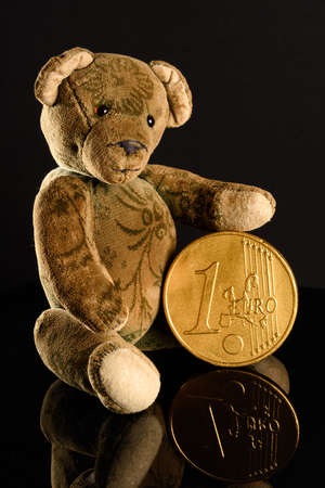 Antique Teddy with a golden 1 Euro coin reflecting on a black base