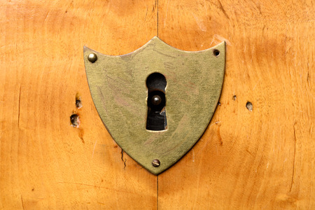 Antique shield-shaped lock on bright cherry wood, frontal view