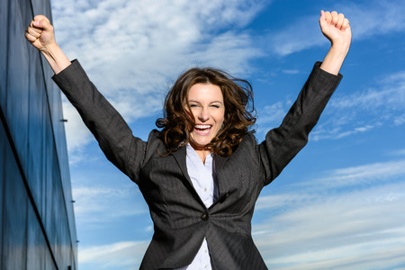 Young Business Woman is jumping for joy in front of blue cloudy sky with office block to the sideの写真素材