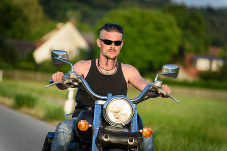 Tough guy with sparrow beard, undercut and blue jeans in motion on the road on a chopper bikeの写真素材