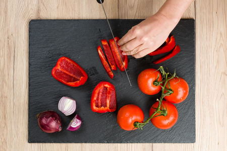 Top down view on black slate cutting board with hands cutting and slicing vegetables.の写真素材