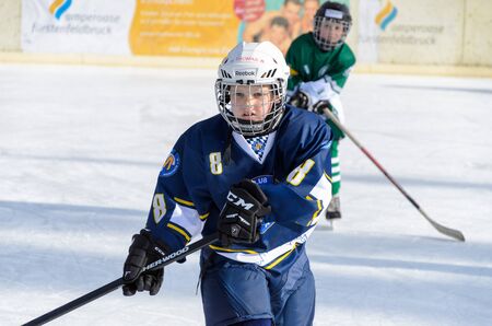 Fuerstenfeldbruck, Bavaria, Germany - 06. February 2016: German Kids playing ice hockey. Age is about 10 years. Blue Player watching his shoot to the goal.のeditorial素材