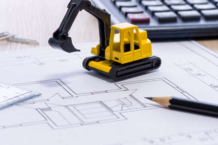 Desktop with blueprint yellow mini excavator, ruler, pencil and calculator symbolizing the wish to build own homeの写真素材