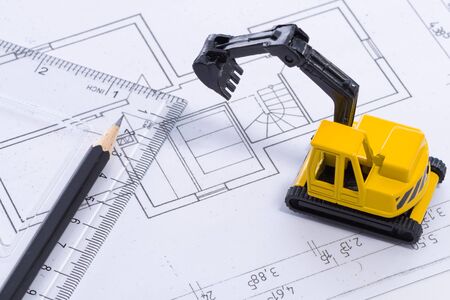 Desktop with blueprint yellow mini excavator, ruler and pencil symbolizing the wish to build own homeの写真素材