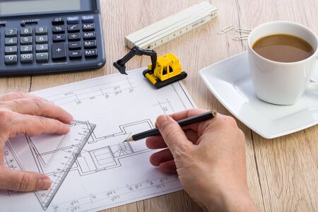 Close-up of architect hands working on a blueprint. Calculator, cup of coffee and miniature...