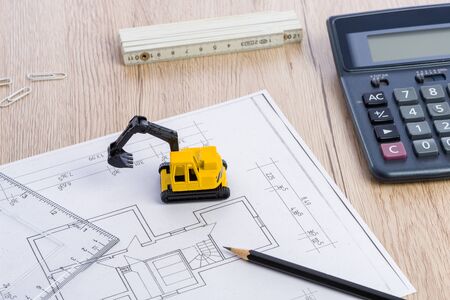 Desktop with blueprint yellow mini excavator, ruler, pencil and calculator symbolizing the wish to build own homeの写真素材
