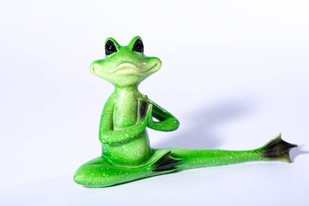 Close up of green frog figure doing meditation and stretching his leg, isolated on whiteの写真素材