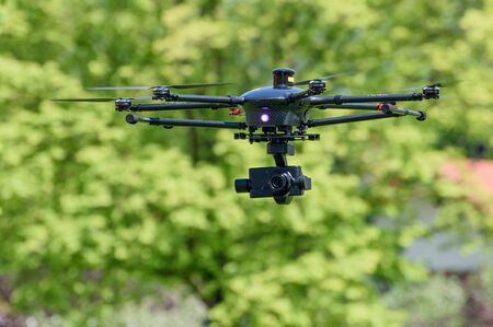 uav drone copter flying with digital camera in front of a tree.