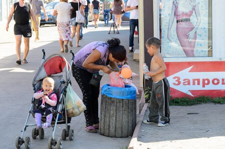 KIEV, UKRAINE ? SEPTEMBER 8, 2016: Woman with three little children searching for food in the waste basket near a market. This shows the gap between rich and poor.のeditorial素材