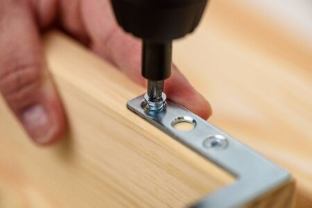 Close up on carpenter hands with cordless screwdriver assembling wooden furniture. Handyman DIY...
