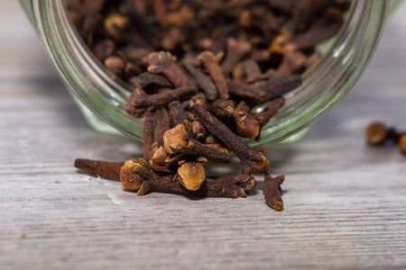 Close up on dried cloves poured from glass on wooden cutting board.の写真素材