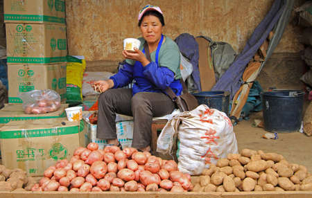 Lijiang, China - June 10, 2015: seller of potato is eating noodle on the market in Lijiang, Chinaのeditorial素材