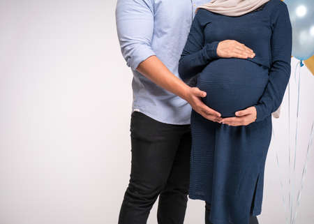 Handsome man and his beautiful pregnant wife are hugging and smiling.の写真素材