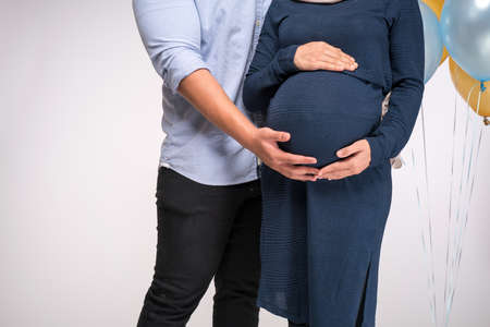 Handsome man and his beautiful pregnant wife are hugging and smiling.の写真素材
