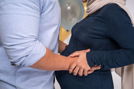 Handsome man and his beautiful pregnant wife are hugging and smiling.の写真素材