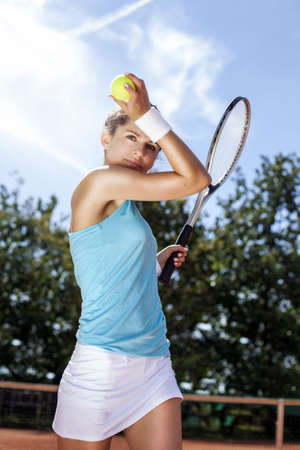 Young girl holding tennis ball on red courtの写真素材