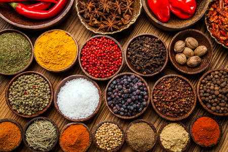 A selection of various colorful spices on a wooden table in bowlsの写真素材