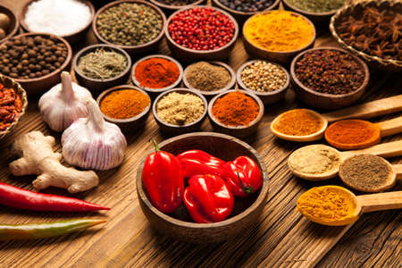 A selection of various colorful spices on a wooden table in bowlsの写真素材