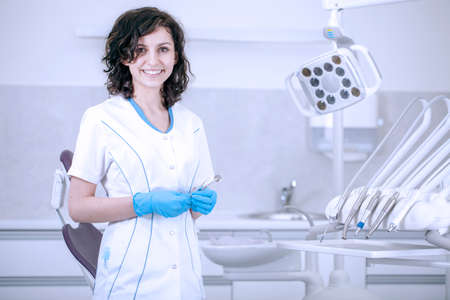 Young professional woman dentist in the office on the background of the chair and dental accessoriesの写真素材