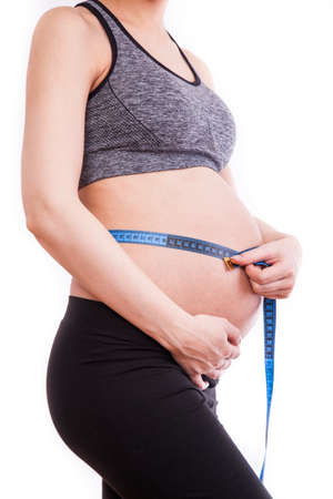 Pregnant woman measures her belly with a measure.の写真素材