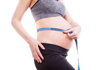 Pregnant woman measures her belly with a measure.の写真素材