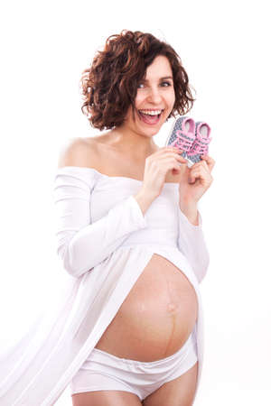 pregnant woman in a white dress holding a tiny baby shoes.の写真素材