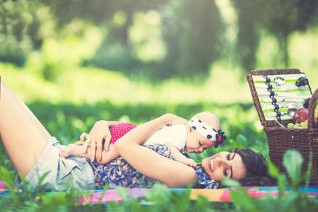 Young beautiful mother sits on blanket with her daughter during a picnic in the parkの写真素材